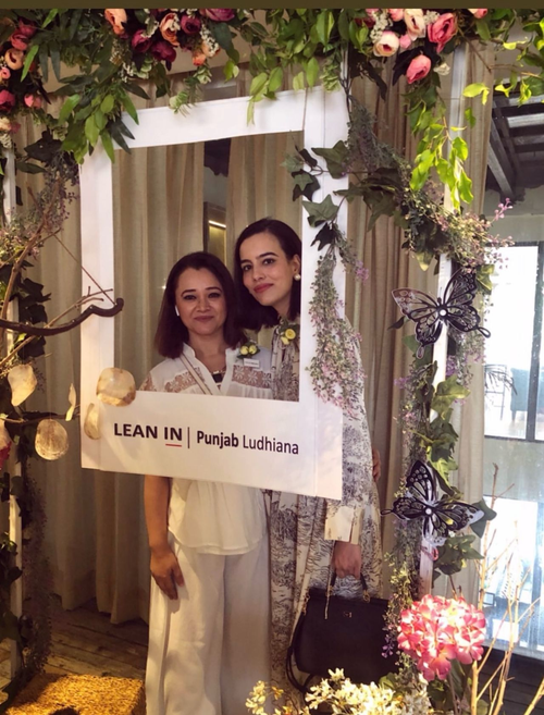 Two women pose together at a Lean In Punjab Ludhiana event, holding a branded photo frame, surrounded by a floral arch with pink roses, greenery, and decorative butterflies.